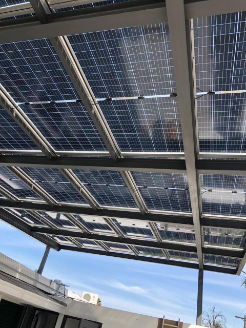 Pérgola solar vista desde abajo: se ven las celdas a través del vidrio trasero de los paneles bifaciales